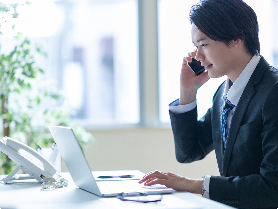 電話をしながらノートパソコンで企業情報を確認する営業担当者
